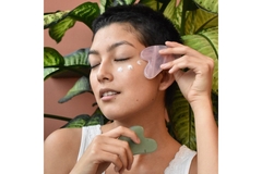 A woman with moisturizer on her cheek and holding a gua sha.
